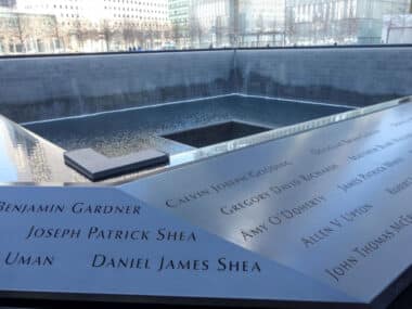 Die Namen der Opfer sind auf einer Metalltafel am 9/11-Memorial in New York City eingraviert, mit Blick auf die großen reflektierenden Becken im Hintergrund.
